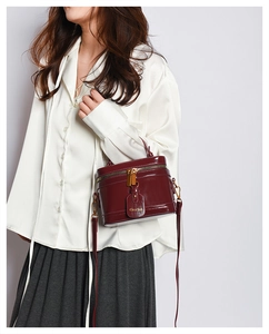 Deep red vintage cylinder bag in glossy patent leather shown on model with shoulder strap