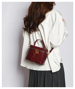 Close-up of burgundy glossy box bag showing metal dual zippers and a detachable shoulder strap