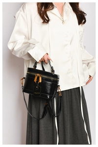 Detail of vintage black leather box bag featuring gold-tone zippers and a hanging brand tag