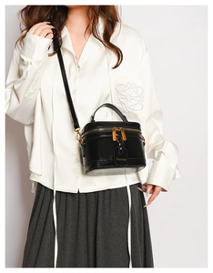 Detail of a black leather vanity box bag with gold zippers and detachable strap