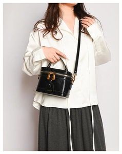 Detail of glossy black box bag with golden hardware and adjustable leather shoulder strap