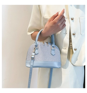 Detail of light blue shell bag with textured twill and smooth leather finish held by model