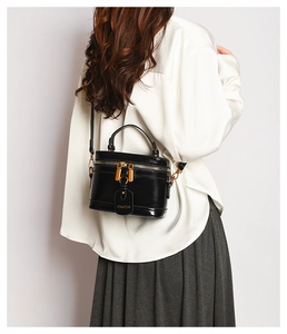 Rear view of a model wearing a black glossy box bag with gold double zippers