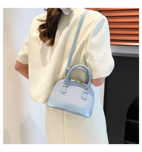 Light blue shell-shaped bag with gold hardware shown on a model in a modern home setting