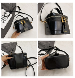 Macro detail of black leather box bag featuring gold-tone zippers and adjustable strap