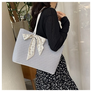 Close-up of woven tote bag with houndstooth silk scarf bow and white shoulder strap