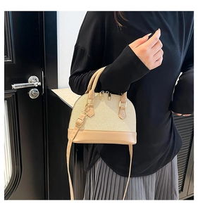 Detail of beige shell bag with woven texture, leather trim and gold zipper rings