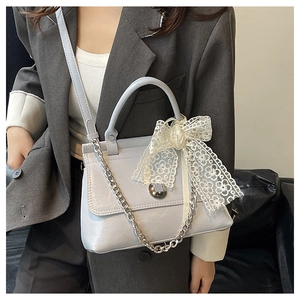 Détail du sac en cuir verni bleu clair avec un nœud en dentelle blanche et fermoir rotatif argenté