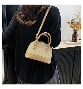 Detail view of beige woven shell bag showing textures, handle, and adjustable shoulder strap