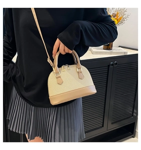 Detail of a minimalist woven shell handbag with beige leather handles and crossbody strap