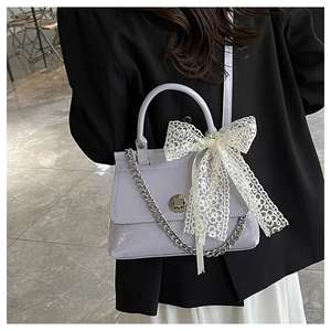 Détail du sac à bandoulière en cuir verni lilas avec nœud en dentelle blanche et fermoir