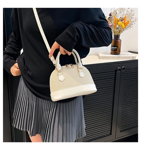 Detail of a beige woven shell handbag with white leather trim and gold hardware in a scene