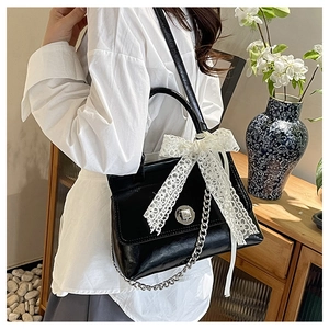 Détail du sac bandoulière noir avec nœud en dentelle blanche et chaîne argent