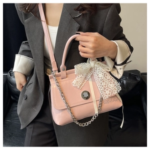 Détail du sac à main rose verni avec un nœud en dentelle et une chaîne argentée