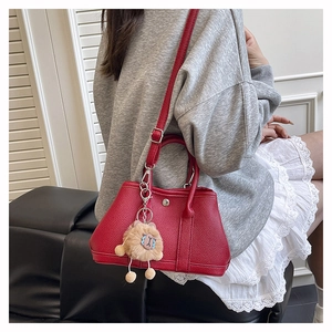 Detail der roten Handtasche aus genarbtem Leder mit Metallschnalle und Plüschanhänger