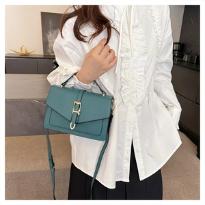 Detailed close-up of teal faux leather handbag with golden buckle and adjustable strap