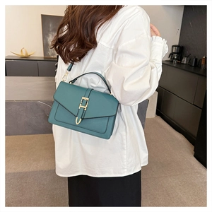 Detail of a deep green crossbody bag with a gold buckle worn on a white shirt