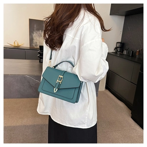 Detail of teal leather square handbag with gold buckle shown on a white shirt
