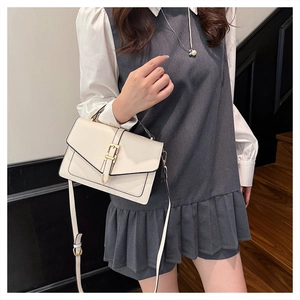 Detail of cream flap square bag with gold buckle and adjustable strap on a model