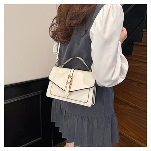 Detail of cream white crossbody bag with gold buckle and black trim on wooden steps