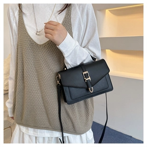 Detailed view of a black crossbody bag with gold hardware worn on a model's shoulder