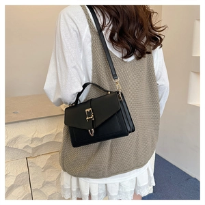 Close-up of black leather square handbag with gold buckle and top handle detail