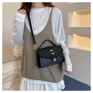 Detail view of high-quality black leather square bag with gold metal clasp on model