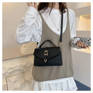 Detail of elegant black crossbody bag featuring a gold rectangular buckle on a model