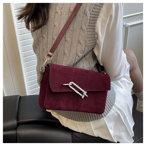 Detail of burgundy suede crossbody bag featuring a distinctive silver metal clasp closure