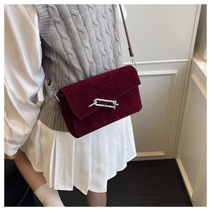 Detail of burgundy suede crossbody bag with metallic clasp worn by a model