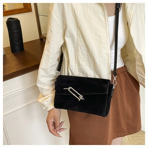 Detail of a black suede crossbody bag featuring a large silver U-shaped metal buckle