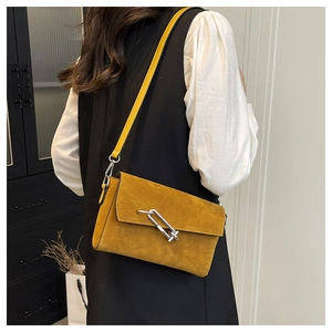 Detail view of mustard yellow suede crossbody bag with silver link chain lock on model