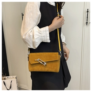 Detail of yellow suede crossbody bag with silver pin lock on a model in black and white outfit