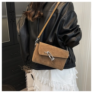 Detail of a brown suede crossbody bag with silver link clasp worn by a fashion model