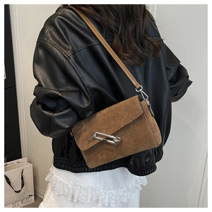 Detail of a brown suede crossbody bag with silver paperclip buckle and leather shoulder strap