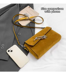 Detail view of mustard yellow suede crossbody bag with metal chain buckle on fabric background