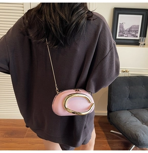Rear view of a model wearing a pink leather crossbody bag with a gold C-shaped metal clasp