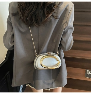 Silver oval evening bag with gold metal clasp shown on a model for scale and style
