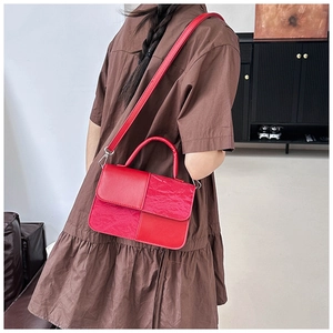 Detail of red paneled handbag with smooth and pleated textures on a model's shoulder