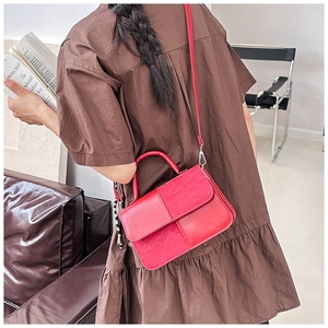 Detailed view of a bright red leather-textured crossbody bag on a brown dress outfit