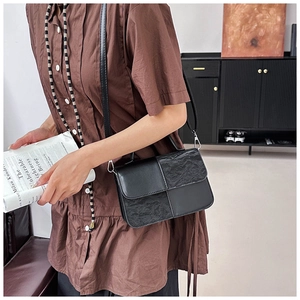 Detailed view of black textured patchwork crossbody bag with adjustable strap and silver buckles