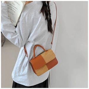 Detail of a textured orange and beige patchwork handbag with silver hardware and strap
