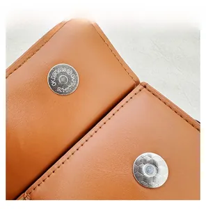 Detail view of silver magnetic buckles and precise stitching on brown leather shoulder bag