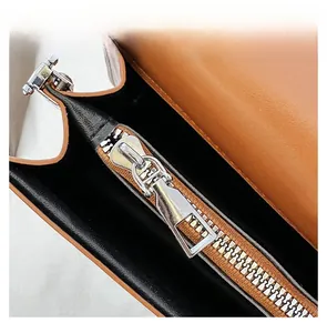 Close-up of smooth silver zipper and lychee pattern leather texture on brown handbag