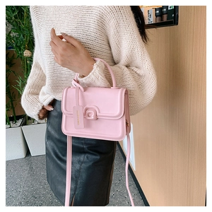 Detailed view of pink crossbody bag with matte finish and fashion logo tag worn by model