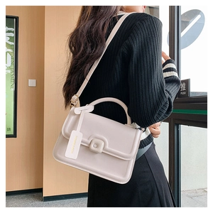 Detail of cream crossbody bag with gold hardware and fashion tag in a cafe setting