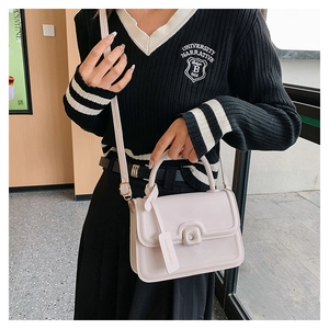 Close-up of beige leather crossbody bag with square metal buckle on striped sweater