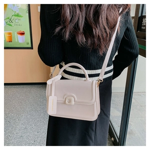 Detail of a cream faux leather crossbody bag with top handle and brand tag on a model