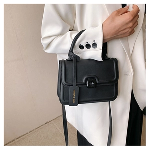 Close-up of black matte leather handbag with square buckle and decorative piping detail