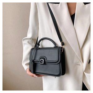 Detailed view of black matte leather handbag featuring unique twist lock and fashion tag